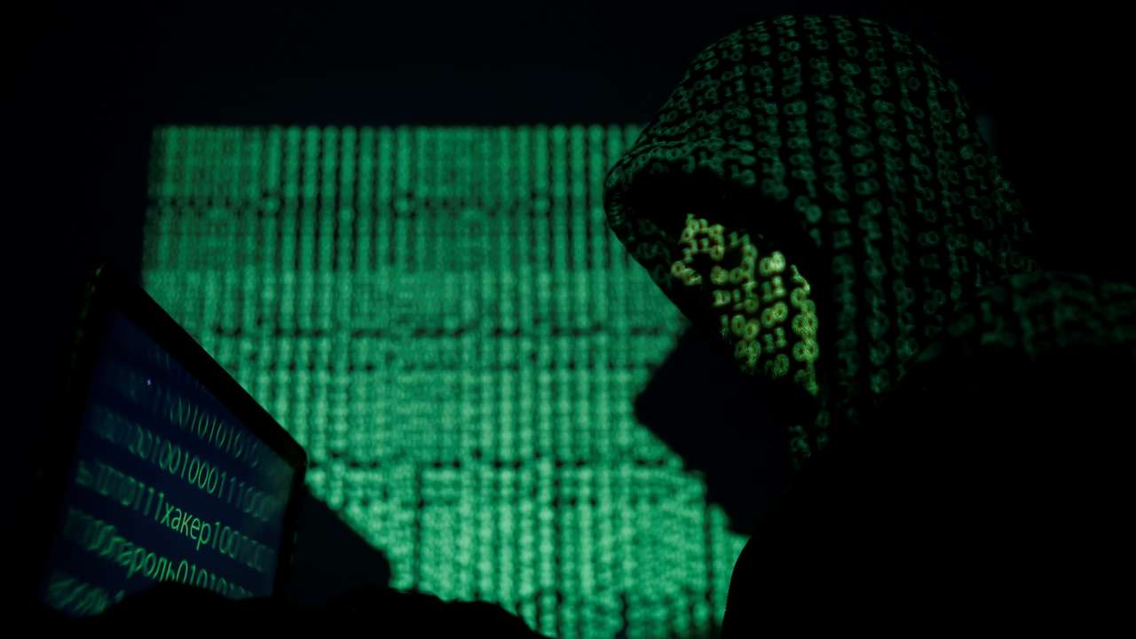Hooded man holds a laptop computer as cyber code is projected on him in this illustration picture