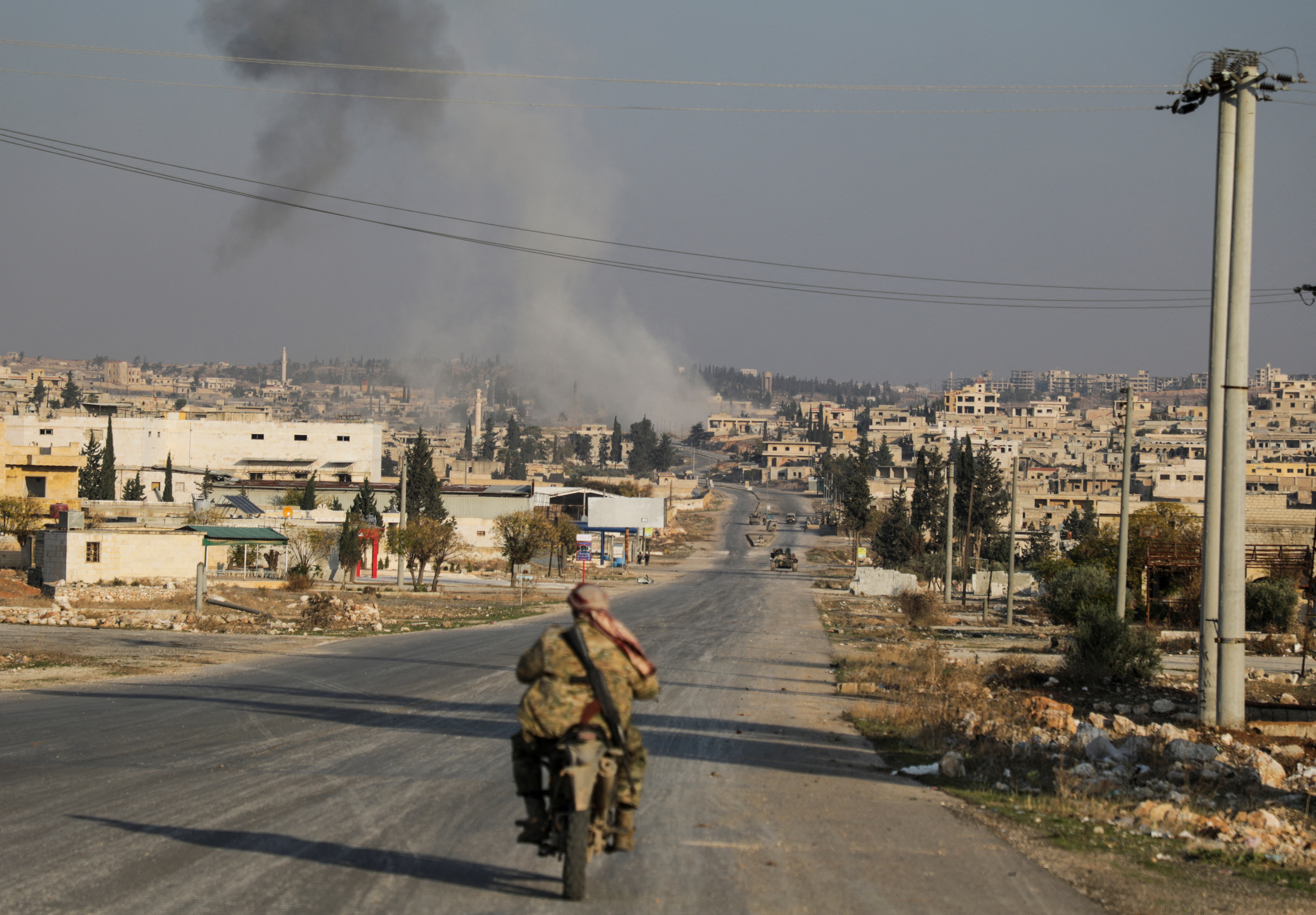 Smoke rises as a member of the rebels led by the Islamist militant group Hayat Tahrir al-Sham drives on a motorbike in al-Rashideen