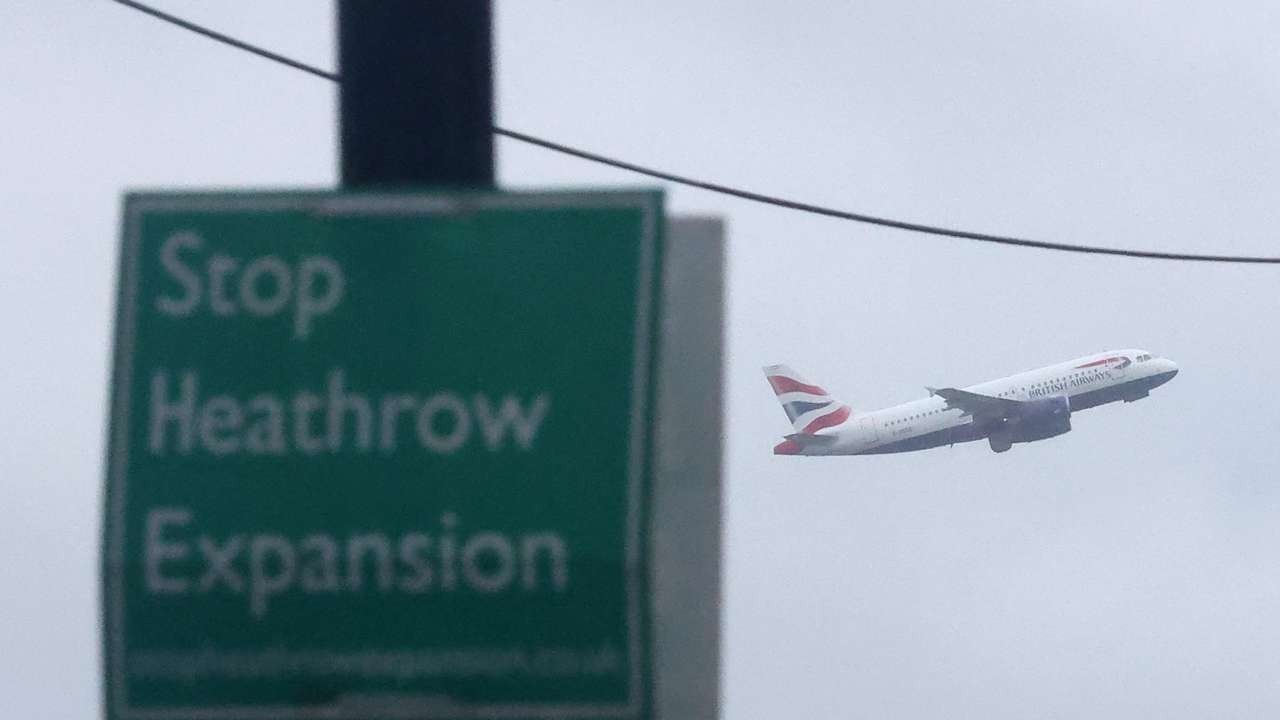 Campaign sign opposing airport development seen attached to lamp post as British Airways passenger plane takes off from Heathrow Airport, Harmondsworth, west London