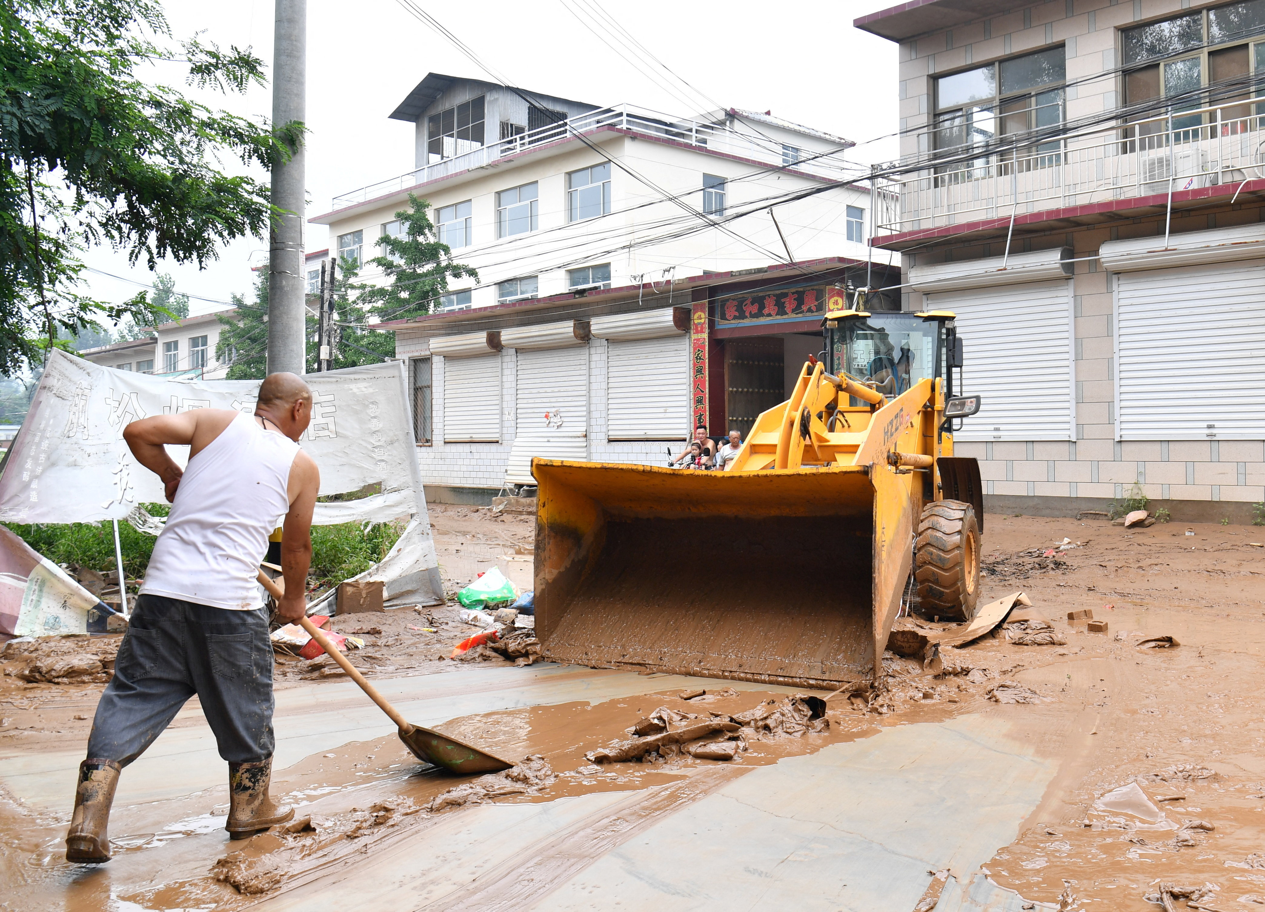 Villagers clear the mud from a street after heavy rainfall flooded Yi county of Baoding