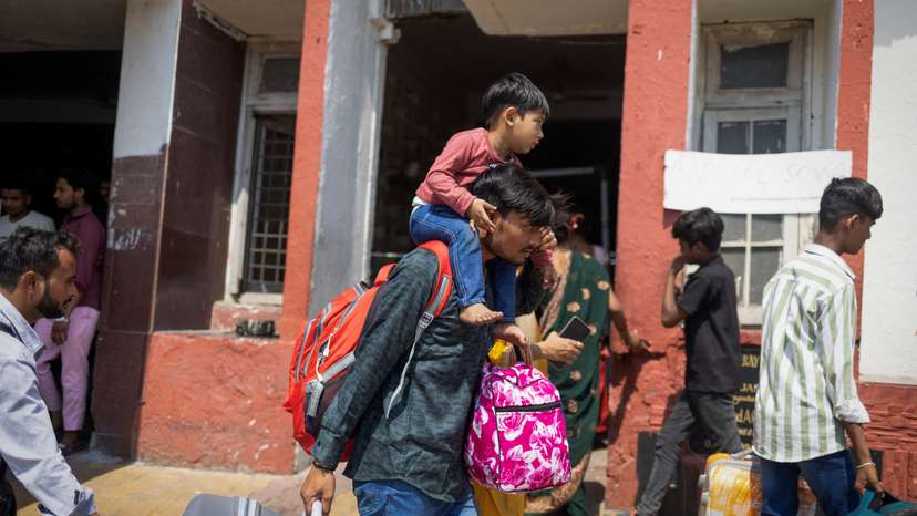 A migrant worker carries his son as he arrives at a railway station to board a train in Jammu