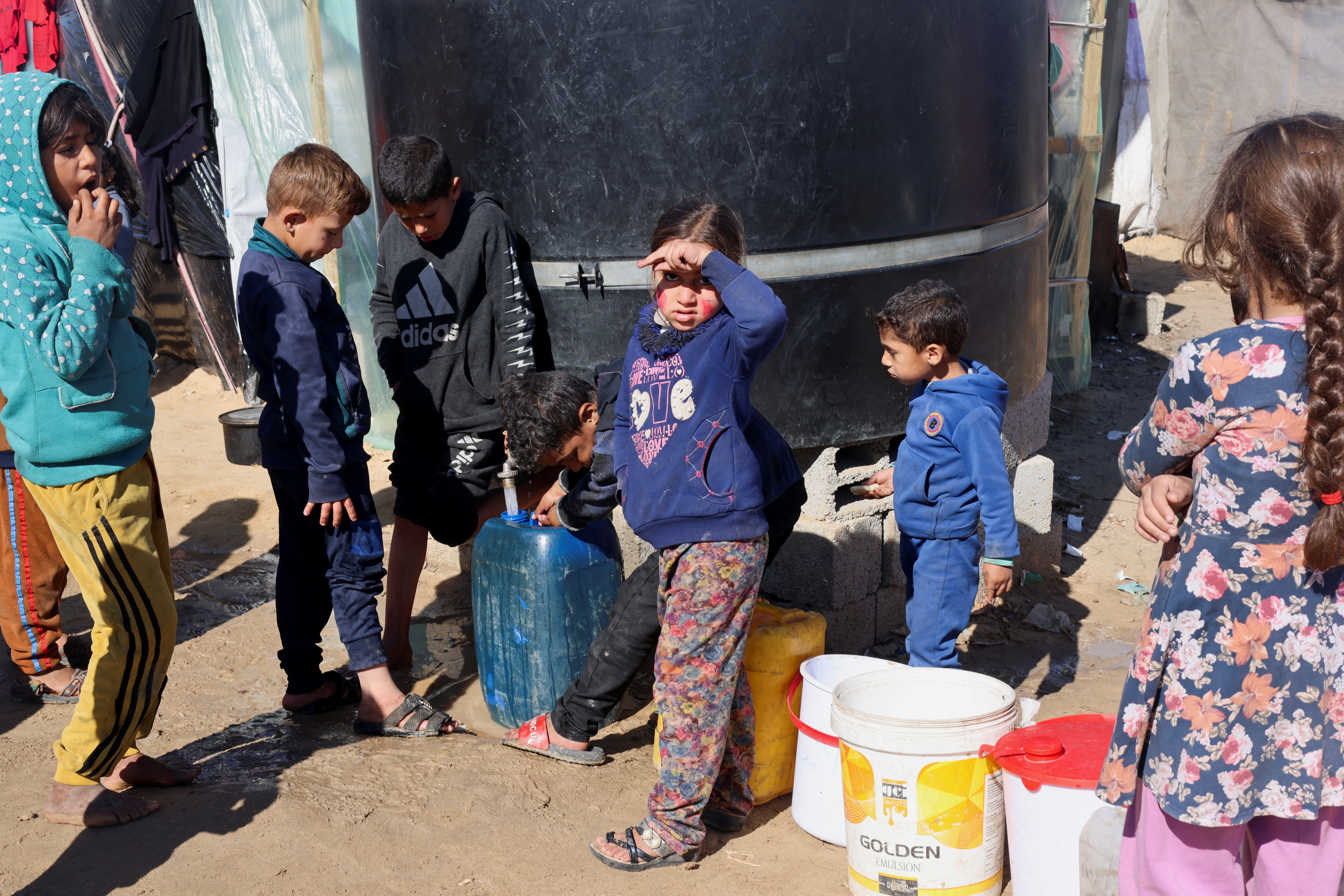 Displaced Palestinian children, who fled their houses due to Israeli strikes, wait to collect water amid shortages, at a tent camp in Rafah