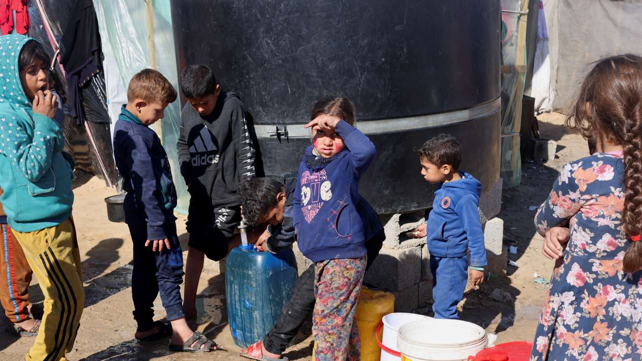 Displaced Palestinian children, who fled their houses due to Israeli strikes, wait to collect water amid shortages, at a tent camp in Rafah