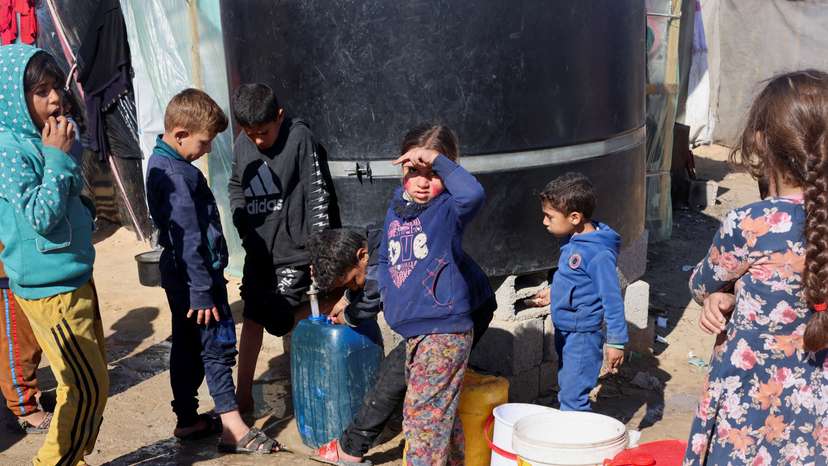 Displaced Palestinian children, who fled their houses due to Israeli strikes, wait to collect water amid shortages, at a tent camp in Rafah
