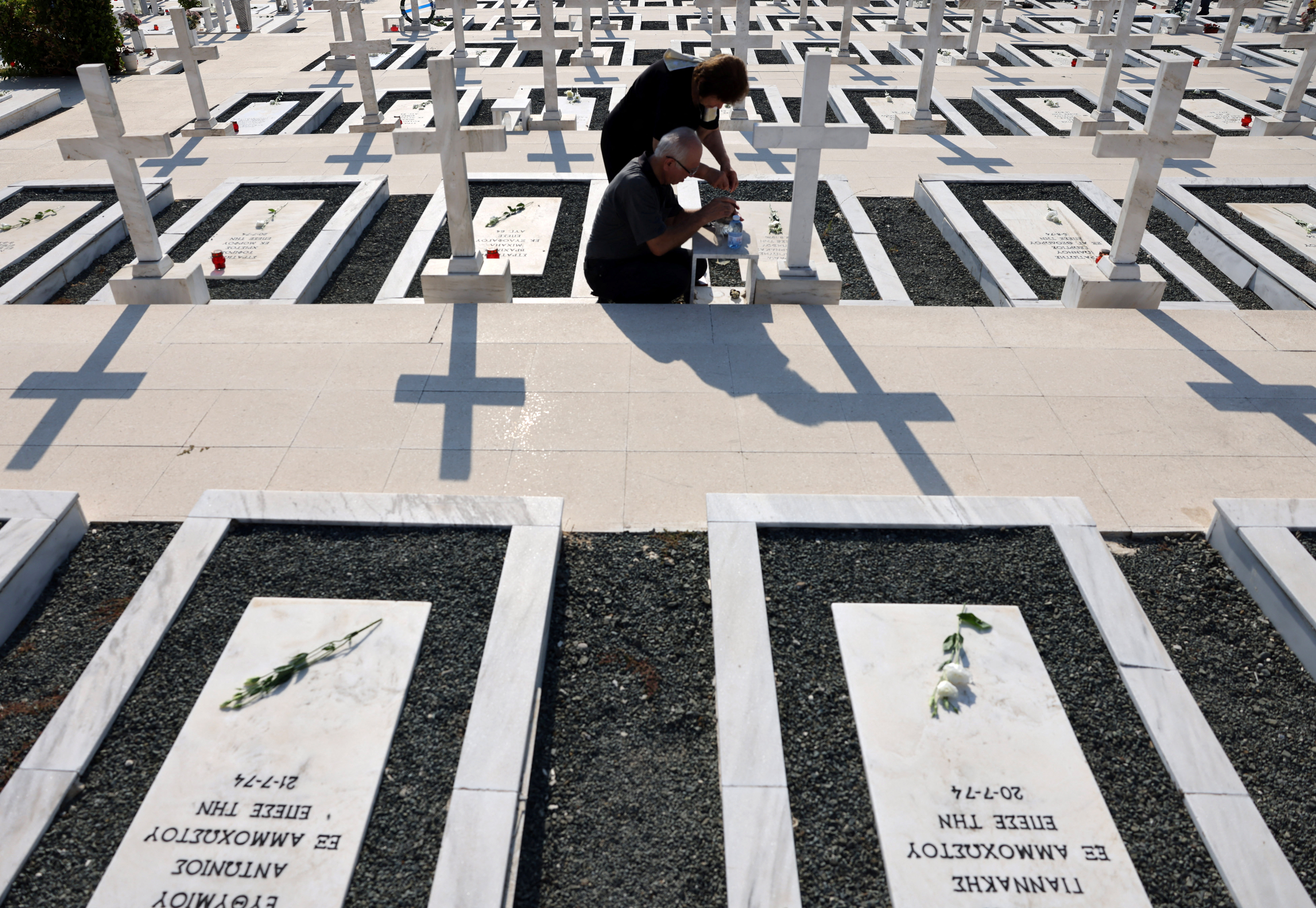 Relatives sit next to the graves of soldiers killed in the 1974 Turkish invasion of Cyprus at the Tymvos Makedonitissas military cemetery in Nicosia