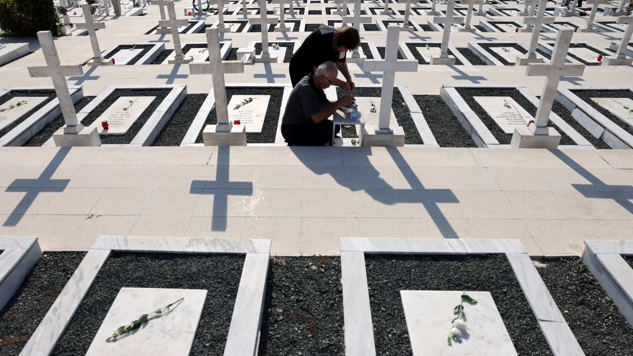 Relatives sit next to the graves of soldiers killed in the 1974 Turkish invasion of Cyprus at the Tymvos Makedonitissas military cemetery in Nicosia