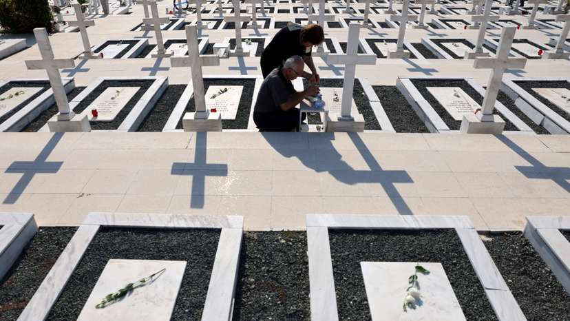 Relatives sit next to the graves of soldiers killed in the 1974 Turkish invasion of Cyprus at the Tymvos Makedonitissas military cemetery in Nicosia