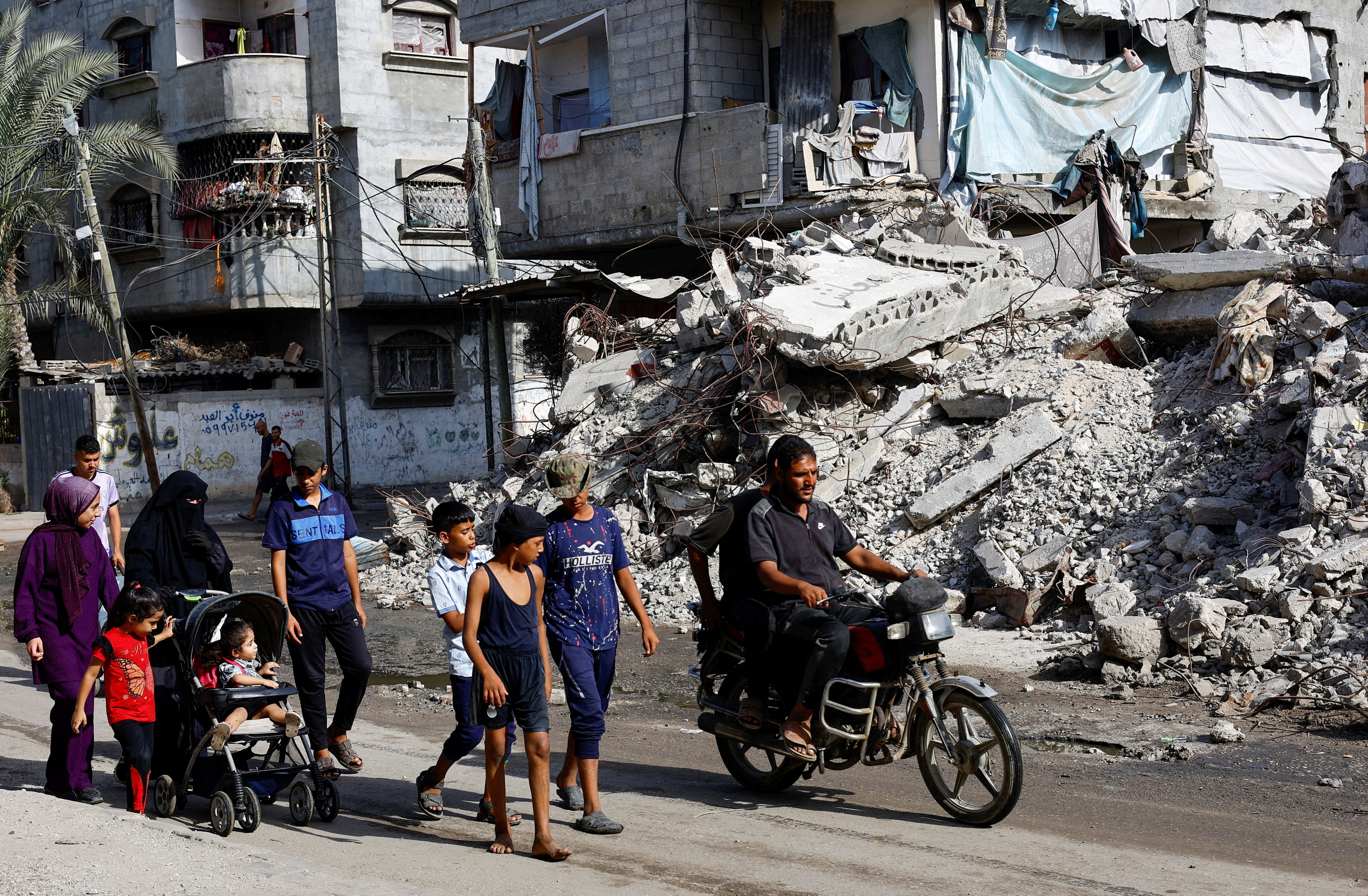 Palestinians walk past a residential building destroyed in previous Israeli strikes, after Hamas agreed to release hostages and accept some other terms in a U.S. plan to end the war, in Nuseirat