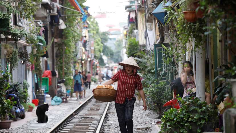 A vendor walks along a railway track as she sells cakes for tourists outside cafes in Hanoi, Vietnam