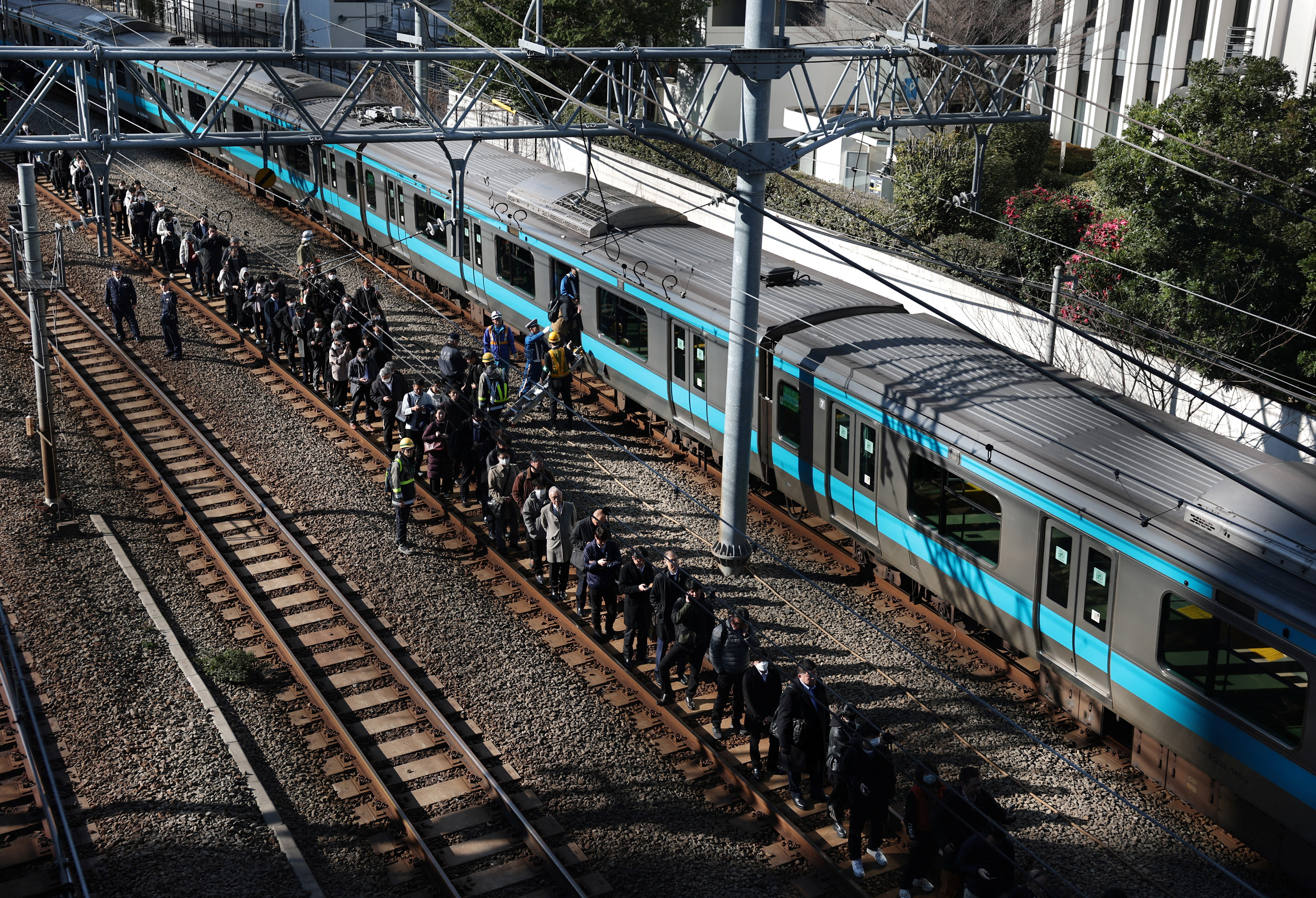 Passengers evacuated from a stranded train on Keihin-Tohoku line stand on a railway track as they head to Tamachi station in Tokyo