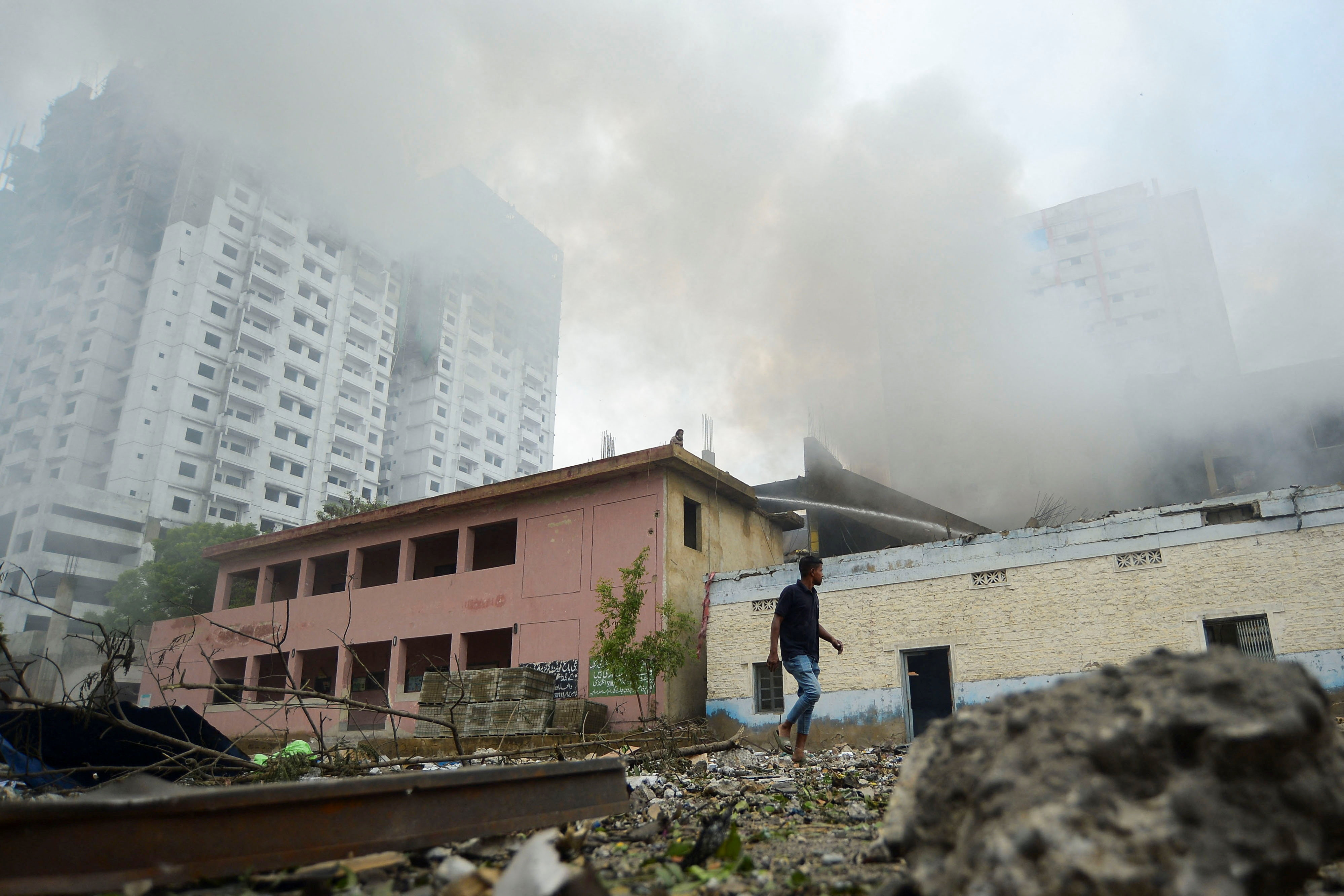 A person walks outside a fireworks warehouse as smoke rises after an explosion, in Karachi