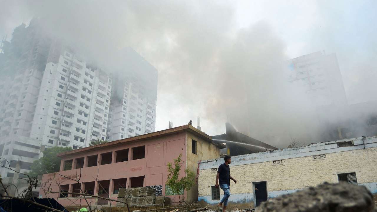 A person walks outside a fireworks warehouse as smoke rises after an explosion, in Karachi