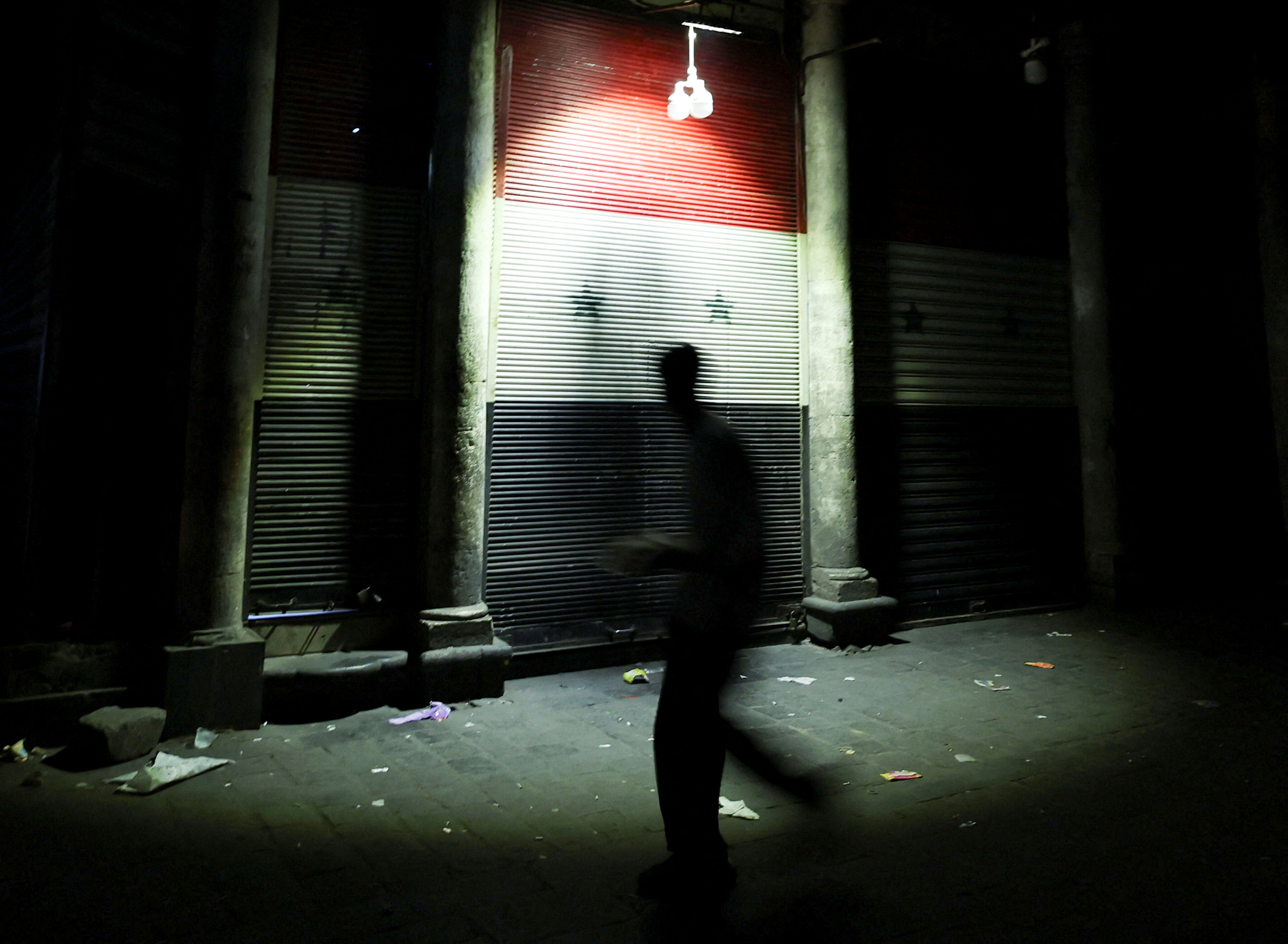 A man walks next to a closed shop painted with a Syrian flag, in Damascus