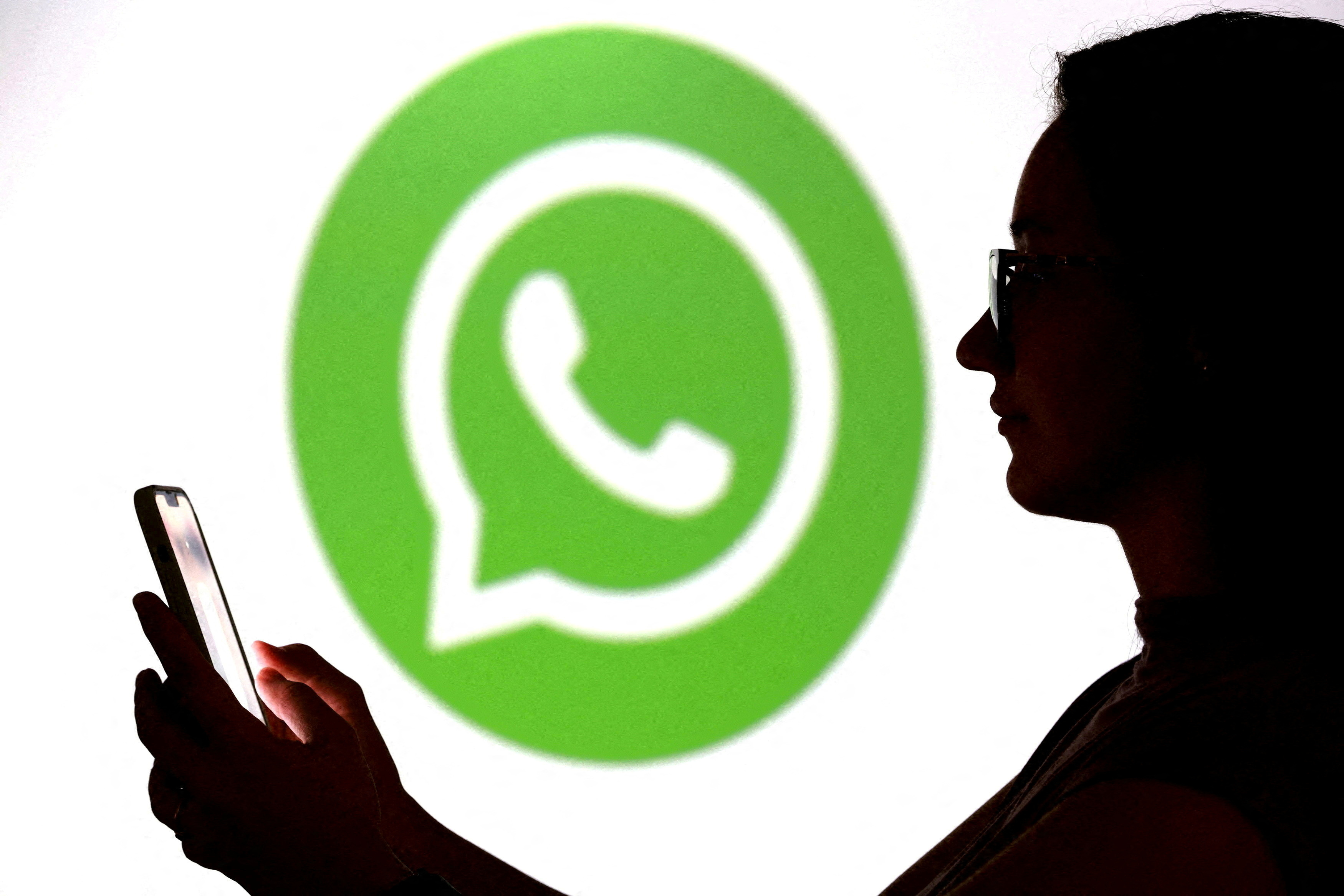 FILE PHOTO: llustration shows a teenager posing for a photo while holding a smartphone in front of a Whatsapp logo