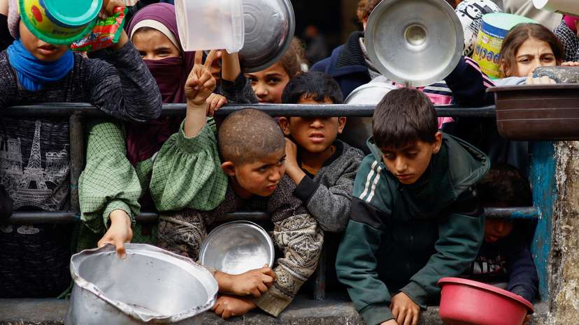 Palestinian children wait to receive food cooked by a charity kitchen amid shortages of food supplies, in Rafah