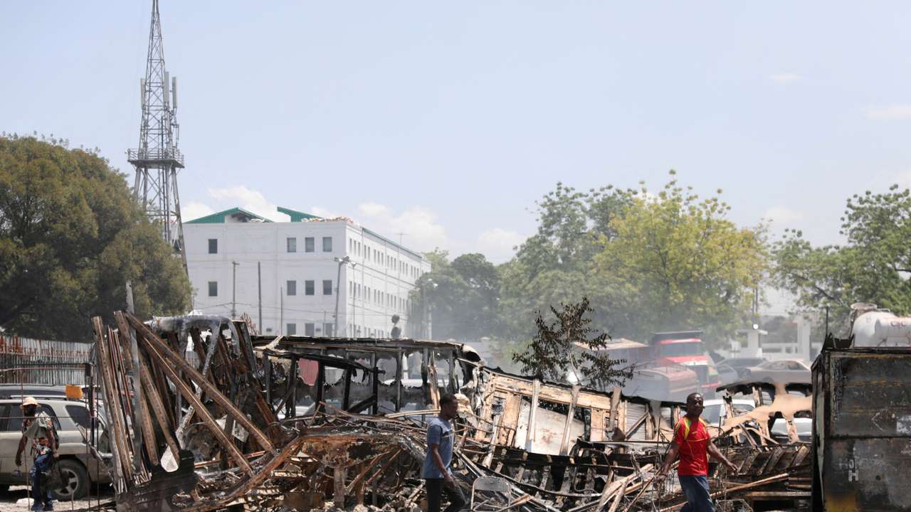 FILE PHOTO: People walk past remains of vehicles after they were set on fire by gangs, in Port-au-Prince