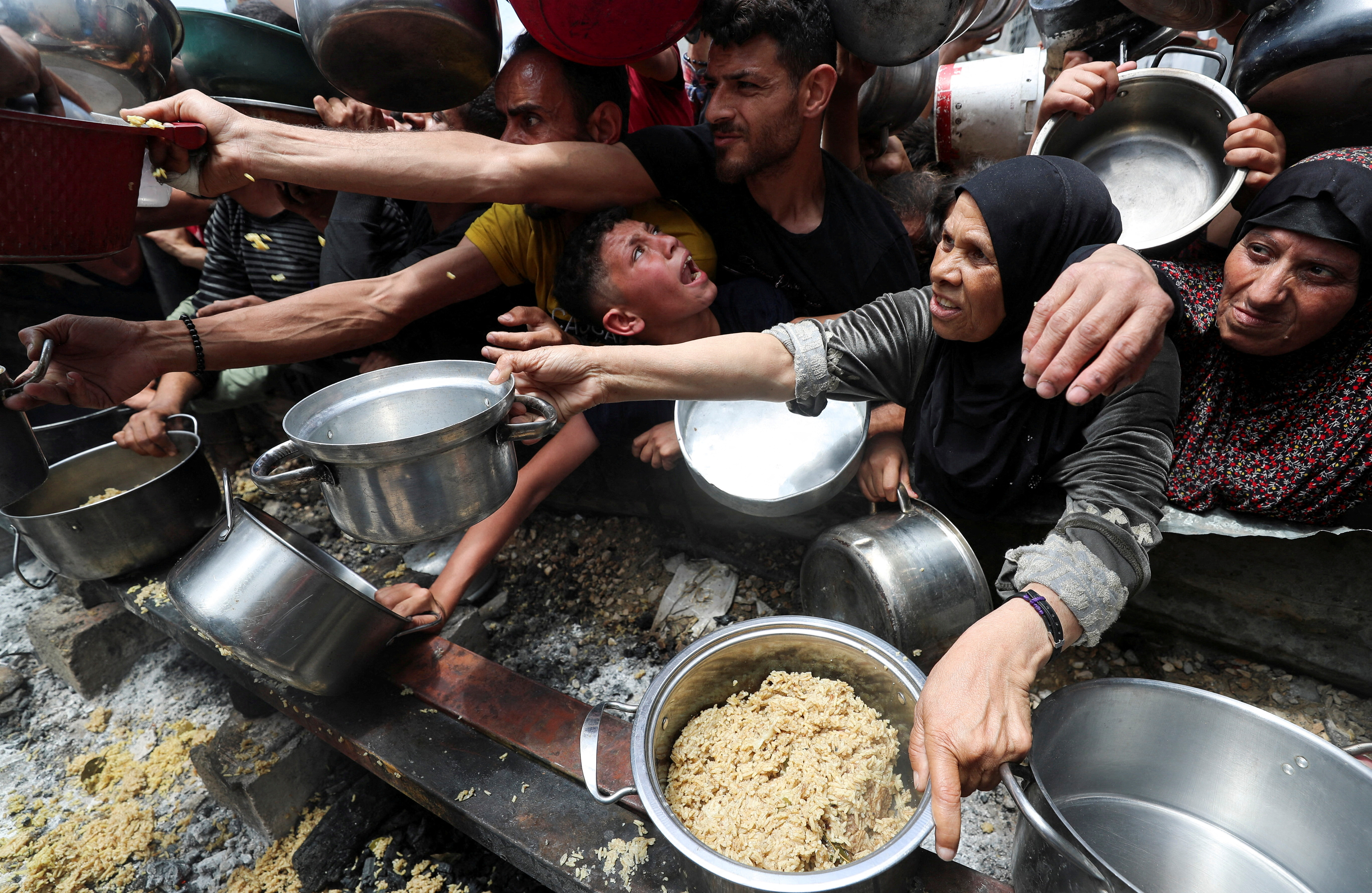 Palestinians wait to receive food cooked by a charity kitchen, in Jabalia