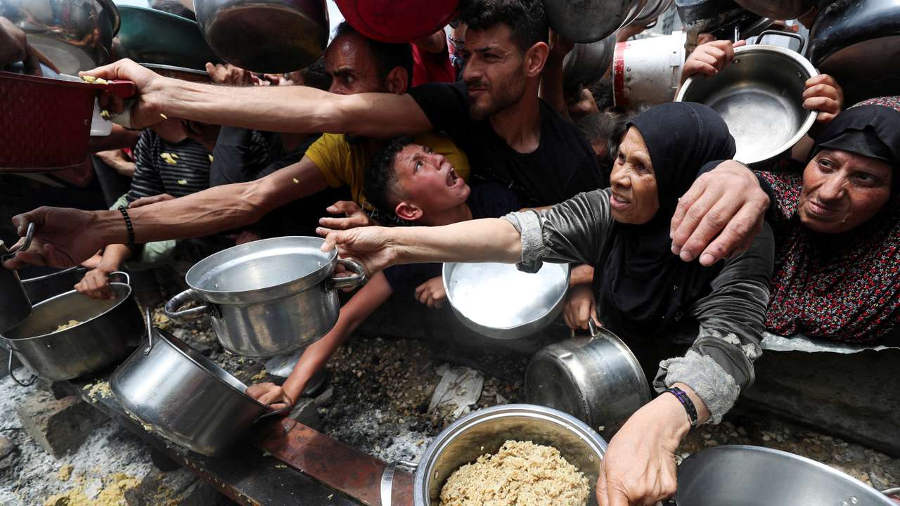 Palestinians wait to receive food cooked by a charity kitchen, in Jabalia
