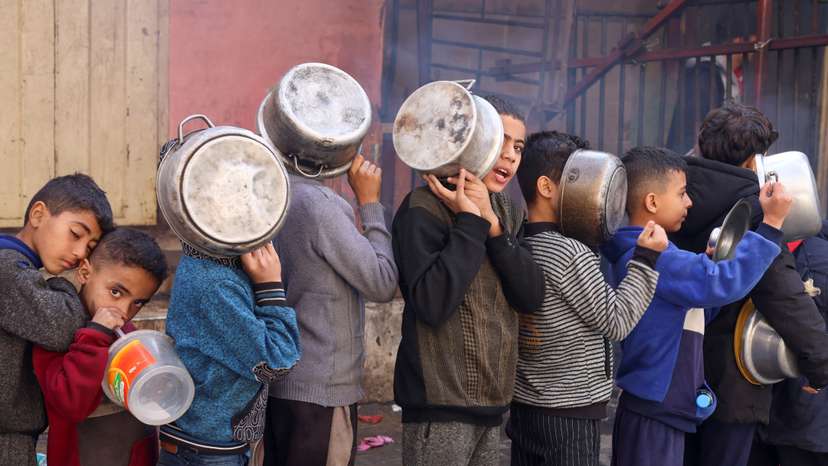 Palestinian children carry pots as they queue to receive food cooked by a charity kitchen, in Rafah in the southern Gaza Strip