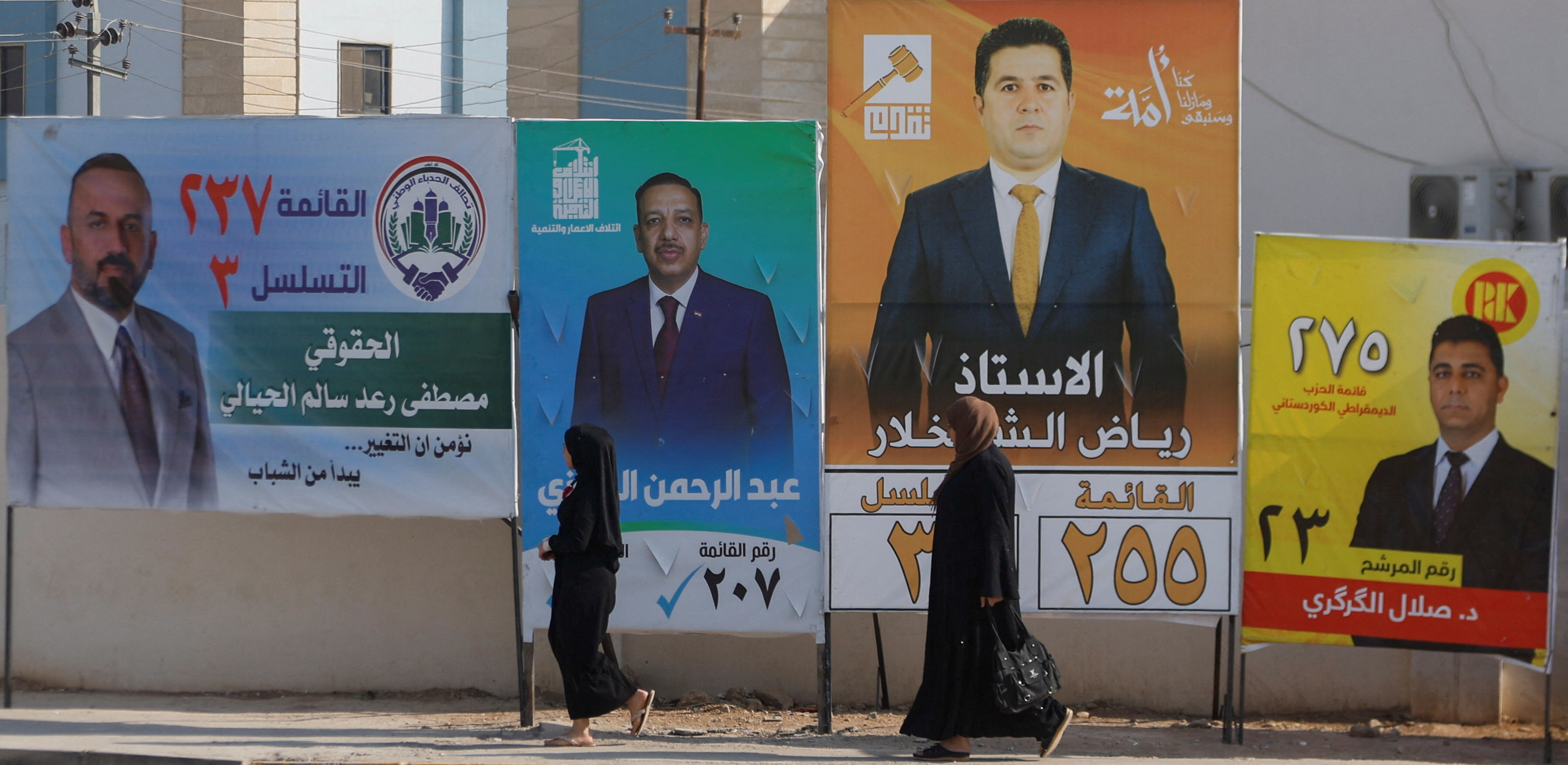 Women walk past campaign posters of candidates ahead of Iraq’s upcoming parliamentary elections in Mosul