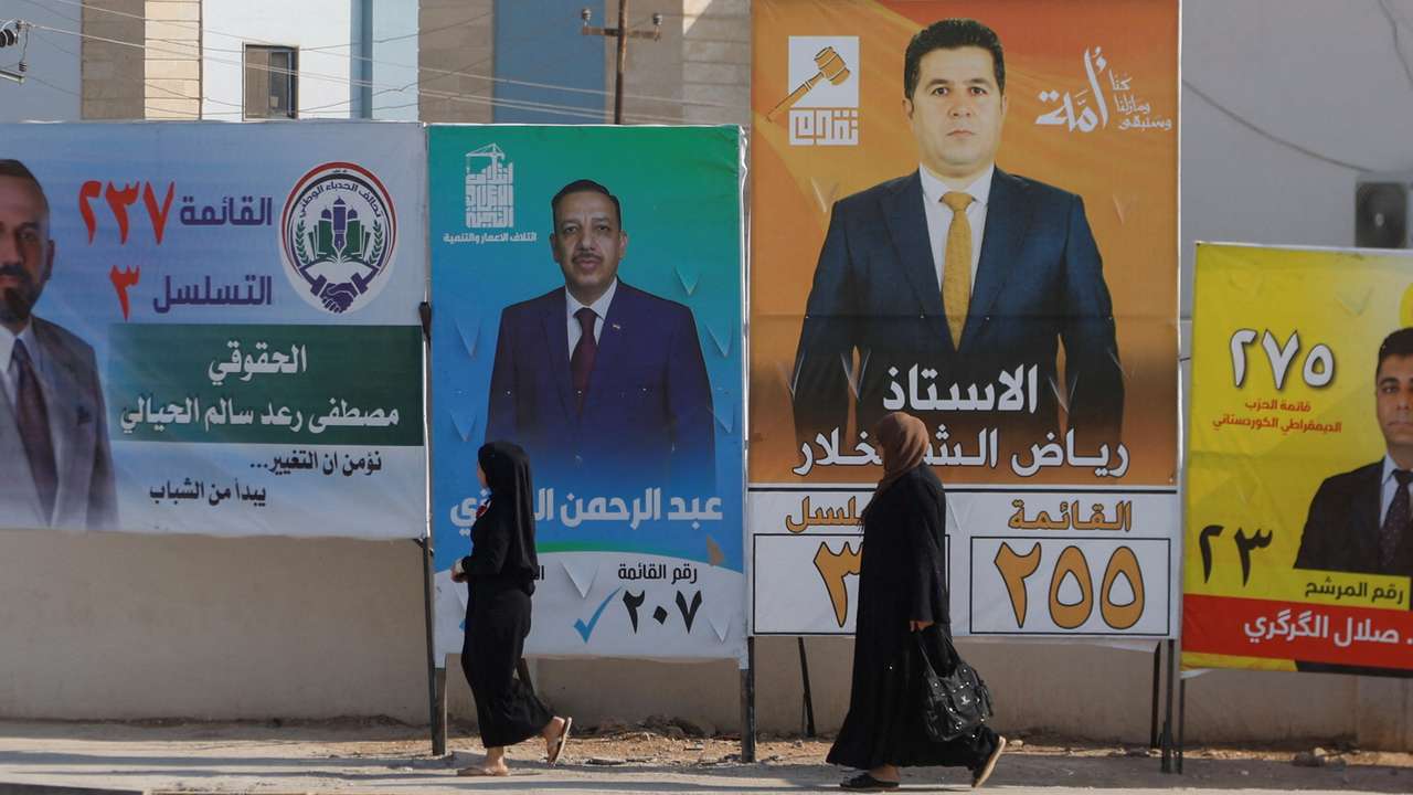 Women walk past campaign posters of candidates ahead of Iraq’s upcoming parliamentary elections in Mosul