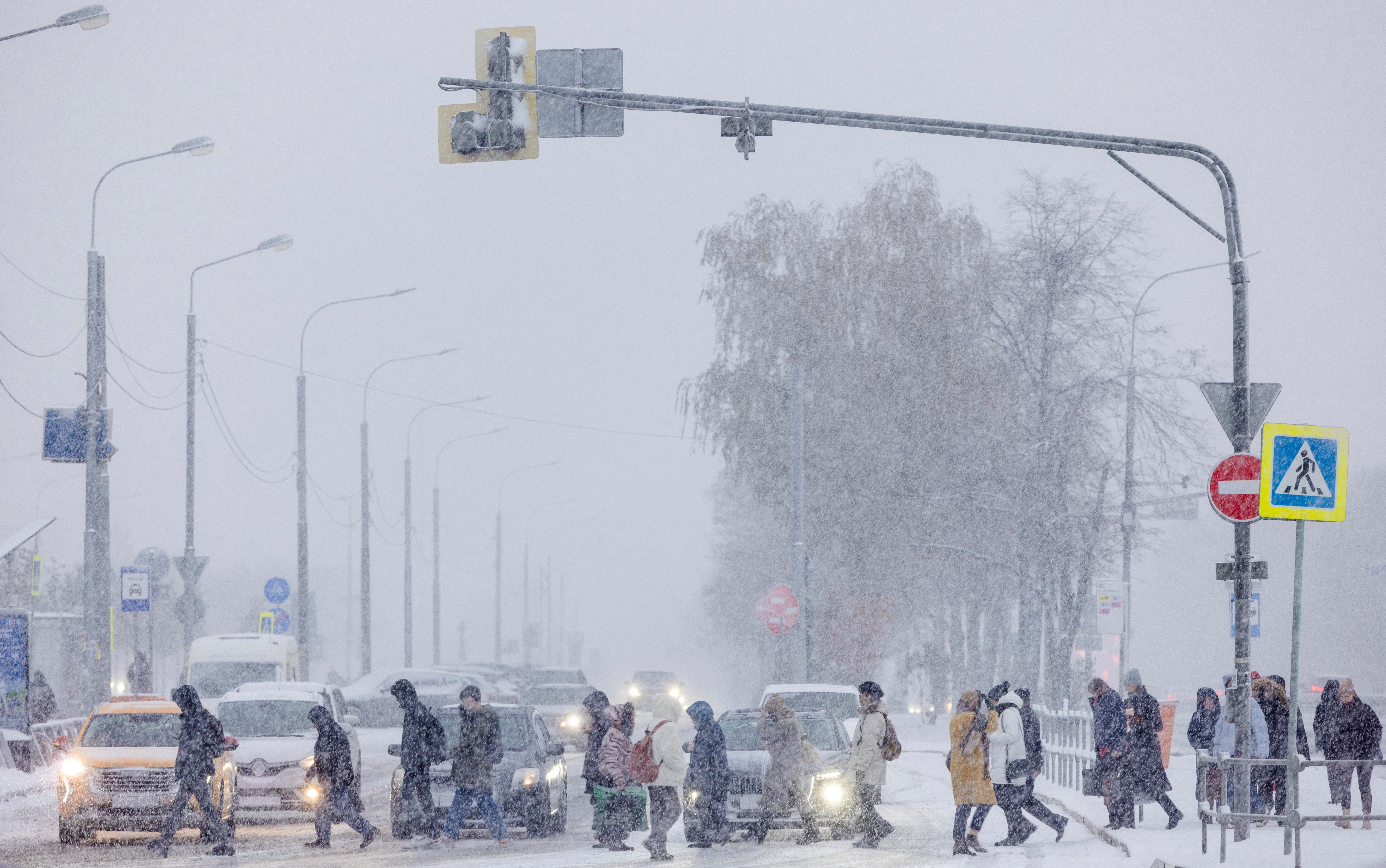 People cross the street during a snowfall on the first snowy day of the season, in Moscow
