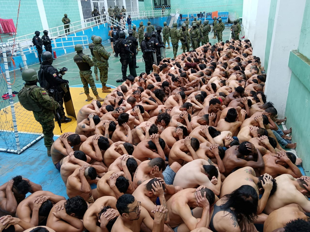 Prisoners sit huddled guarded by police and armed forces in Turi prison, Cuenca