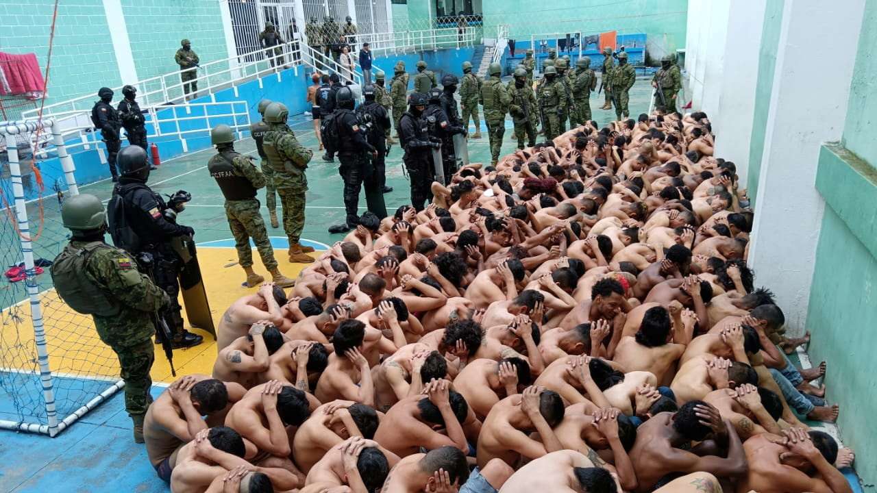 Prisoners sit huddled guarded by police and armed forces in Turi prison, Cuenca