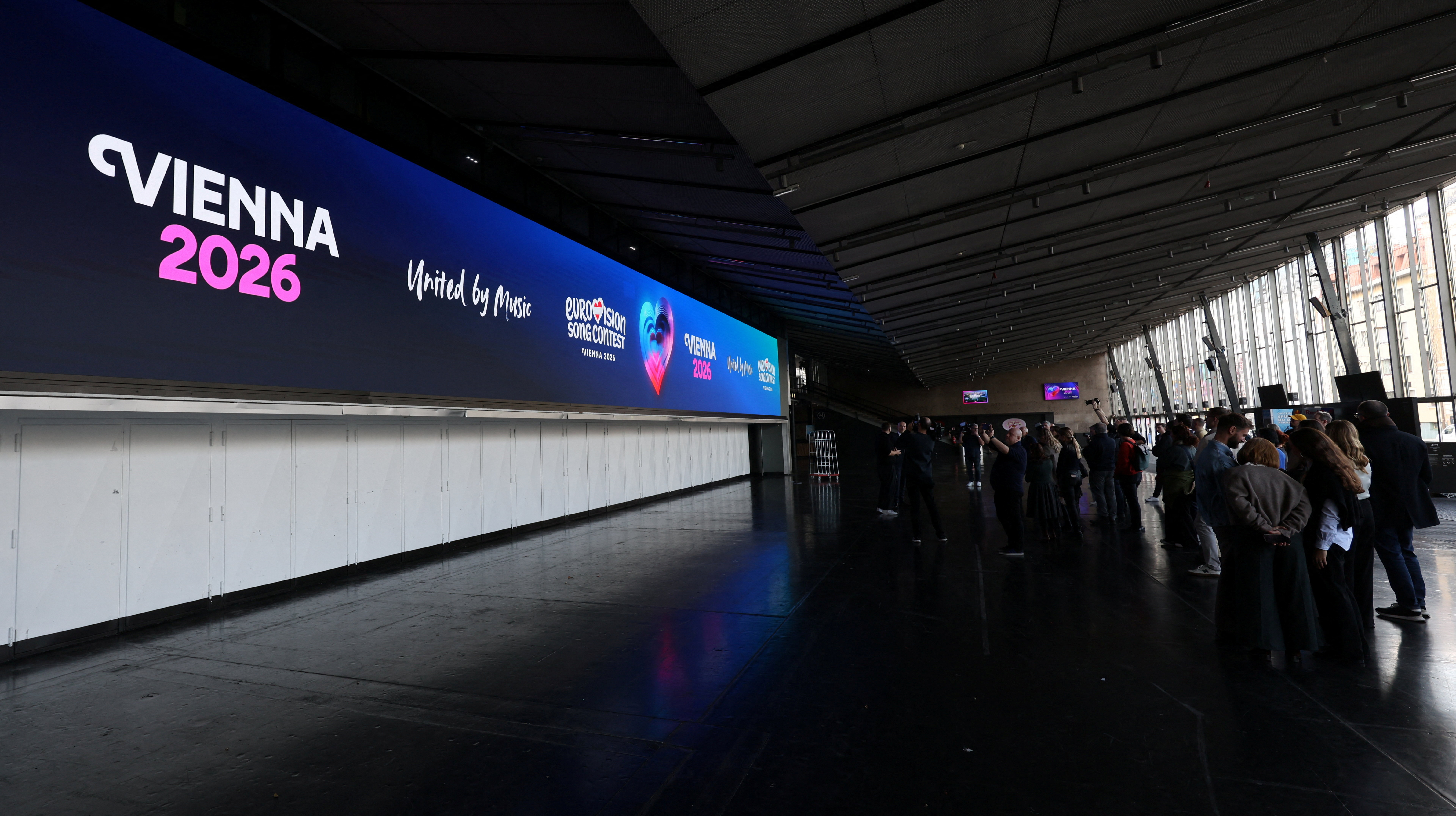 Journalists stand in front of a screen in Wiener Stadthalle, the venue of next year's Eurovision in Vienna