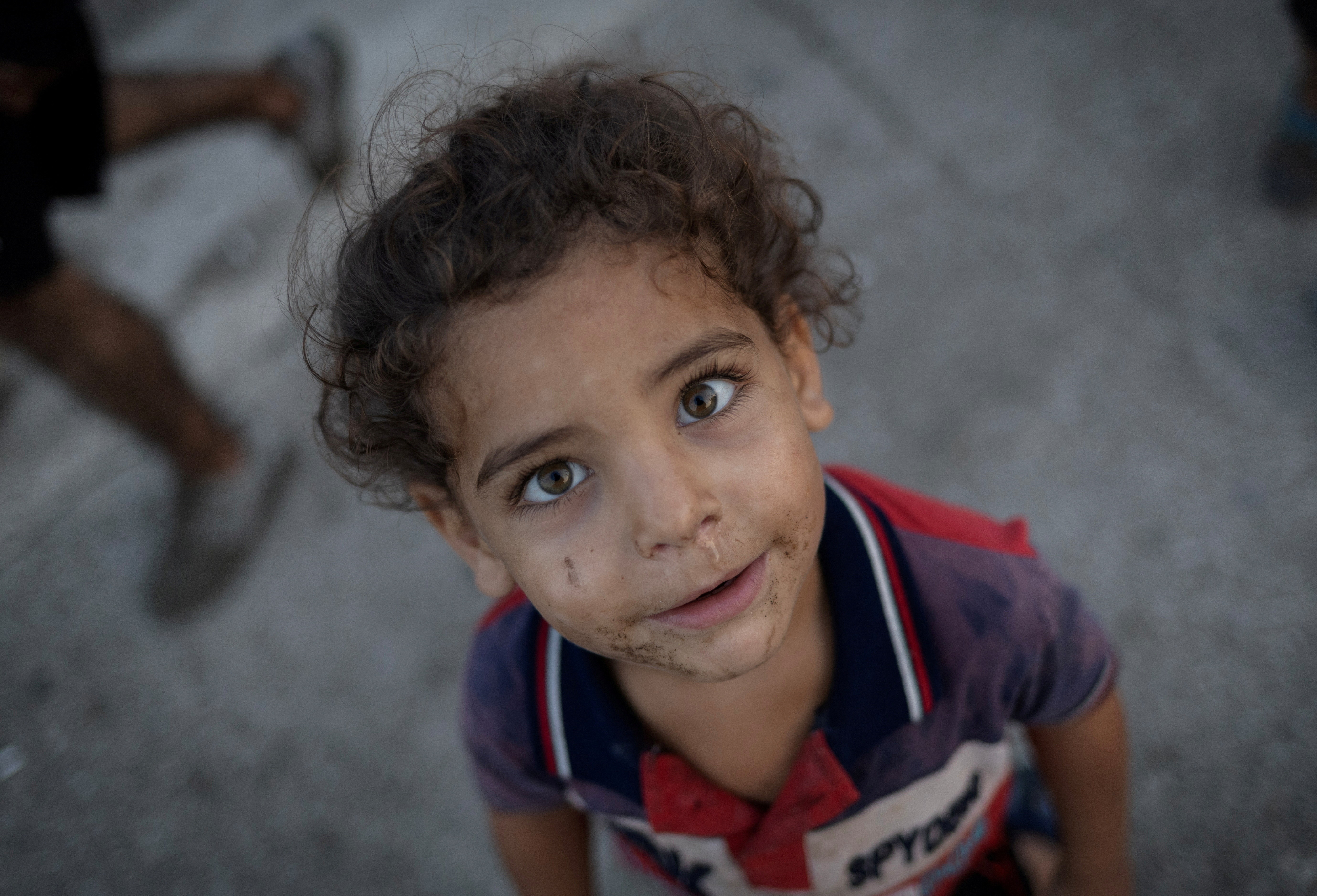 A displaced kid reacts to a camera outside his makeshift shelter at a roadside in Beirut