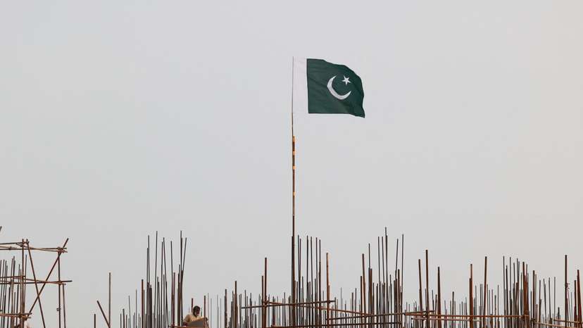 A Pakistani flag flutters over iron scaffoldings as a labourer works at a construction site on the eve of Pakistan's Independence Day celebrations, in Lahore