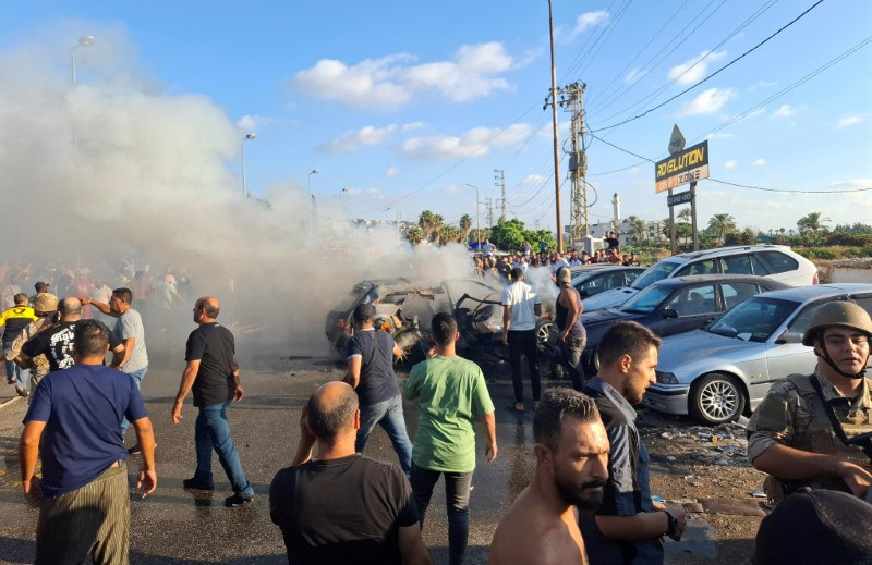 People stand near a burning car in Sidon
