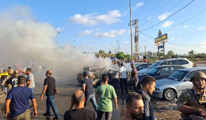 People stand near a burning car in Sidon