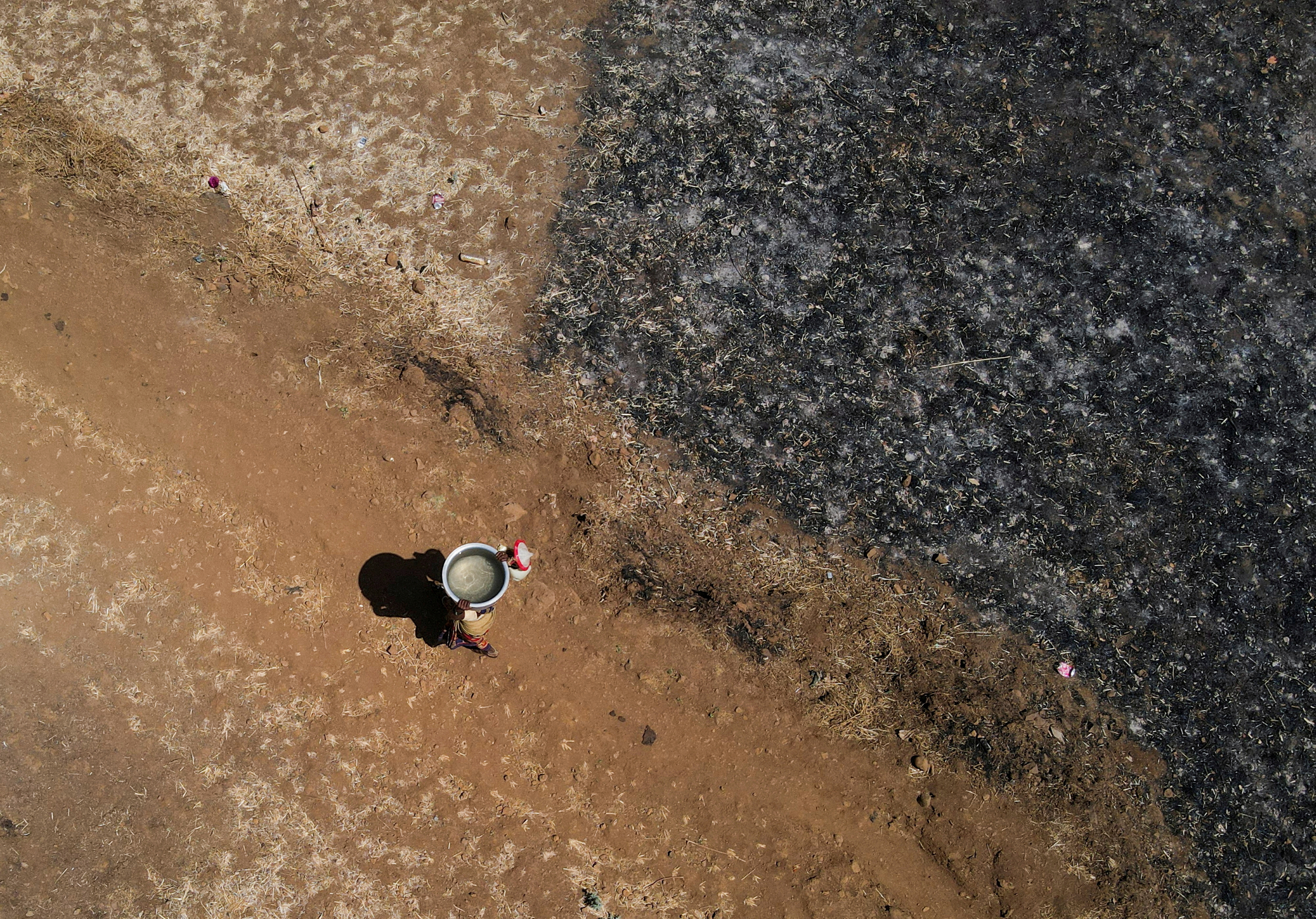 FILE PHOTO: A drone view of a woman carrying a utensil filled with water after drawing it from a well on a hot day in Kasara