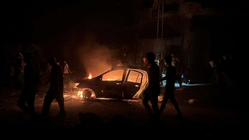 Palestinians walk past a burning car hit in an Israeli strike, in Khan Younis, in the southern Gaza Strip