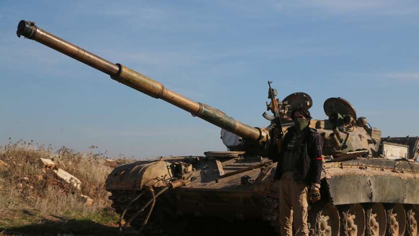 A rebel fighter holds his weapon as he stands in front of a military vehicle in Menagh