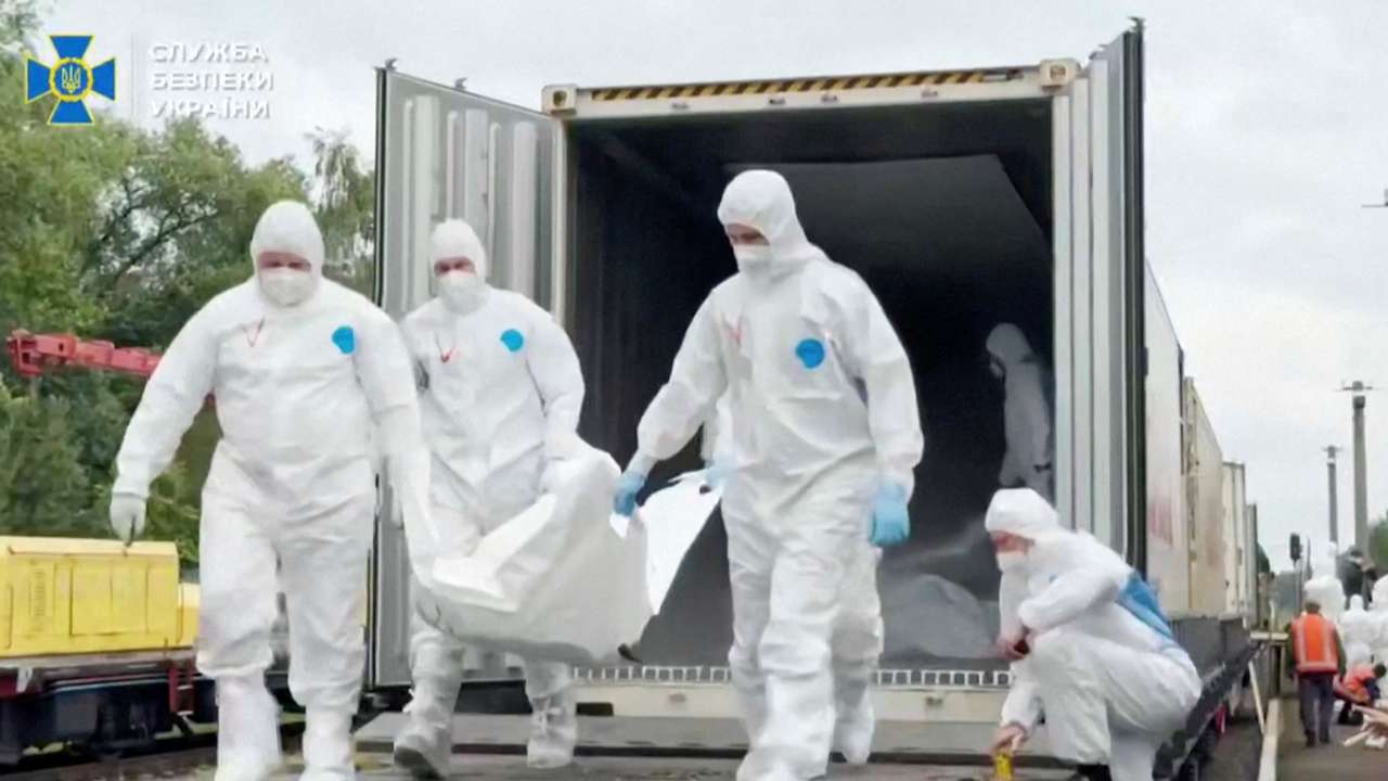 People in hazmat suits carry what is said to be remains of Ukrainian soldiers received from Russia in an unknown location