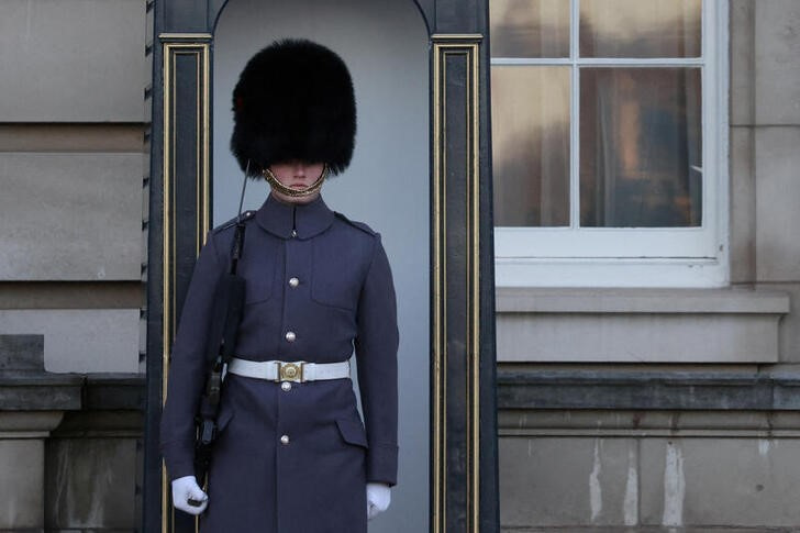 A guard wearing a bearskin cap stands outside Buckingham Palace in London