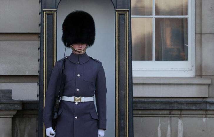 A guard wearing a bearskin cap stands outside Buckingham Palace in London