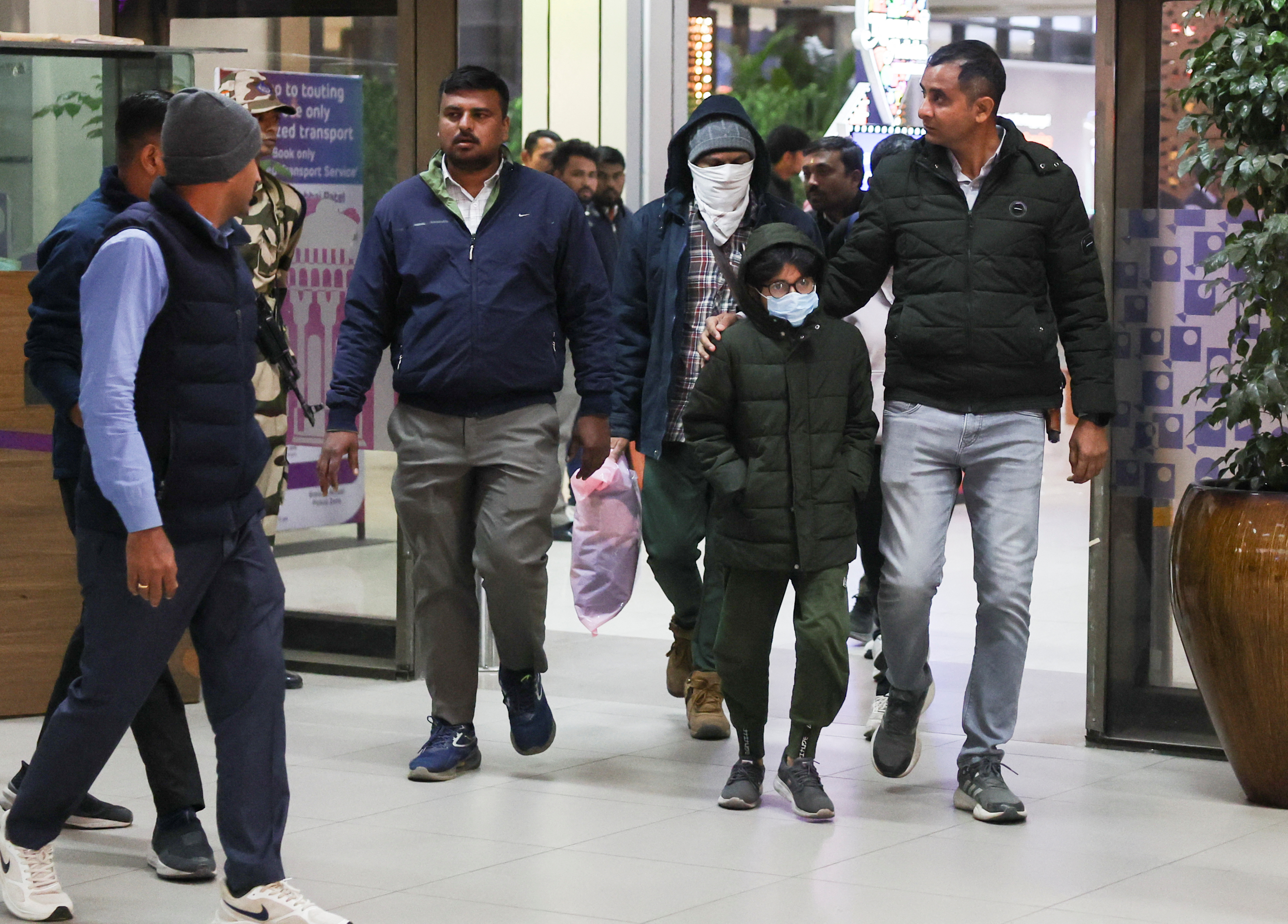 Security personnel escort Indian immigrants deported from the U.S., as they leave the airport in Ahmedabad