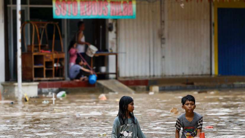 Children wade through water in a flooded residential area following heavy rains in Bekasi