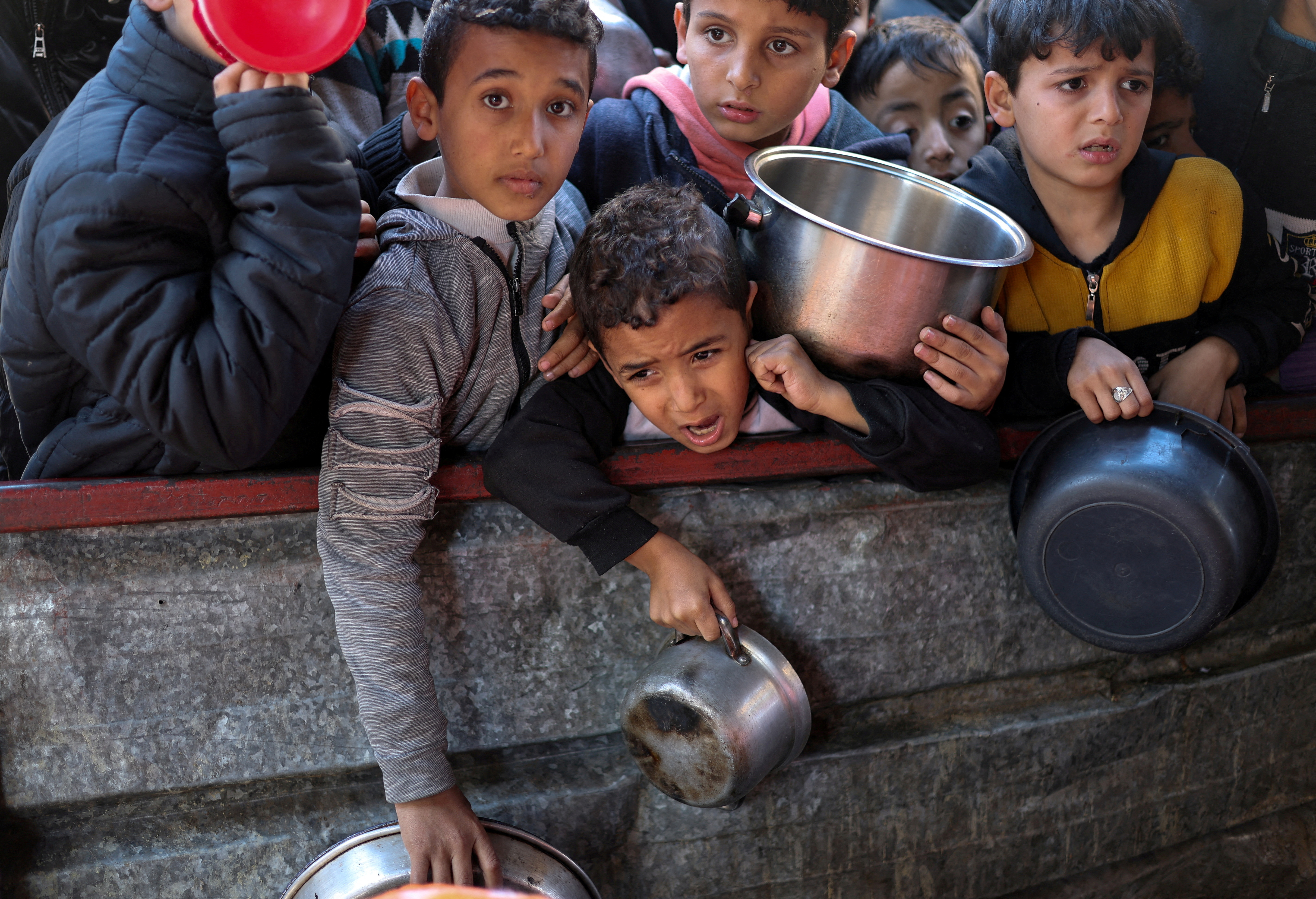 FILE PHOTO: Palestinians wait to receive food cooked by a charity kitchen amid shortages, in Rafah