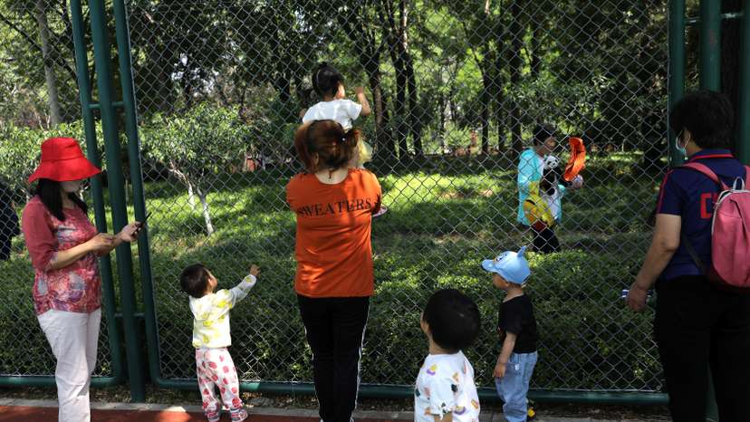 Children play next to adults at a park in Beijing