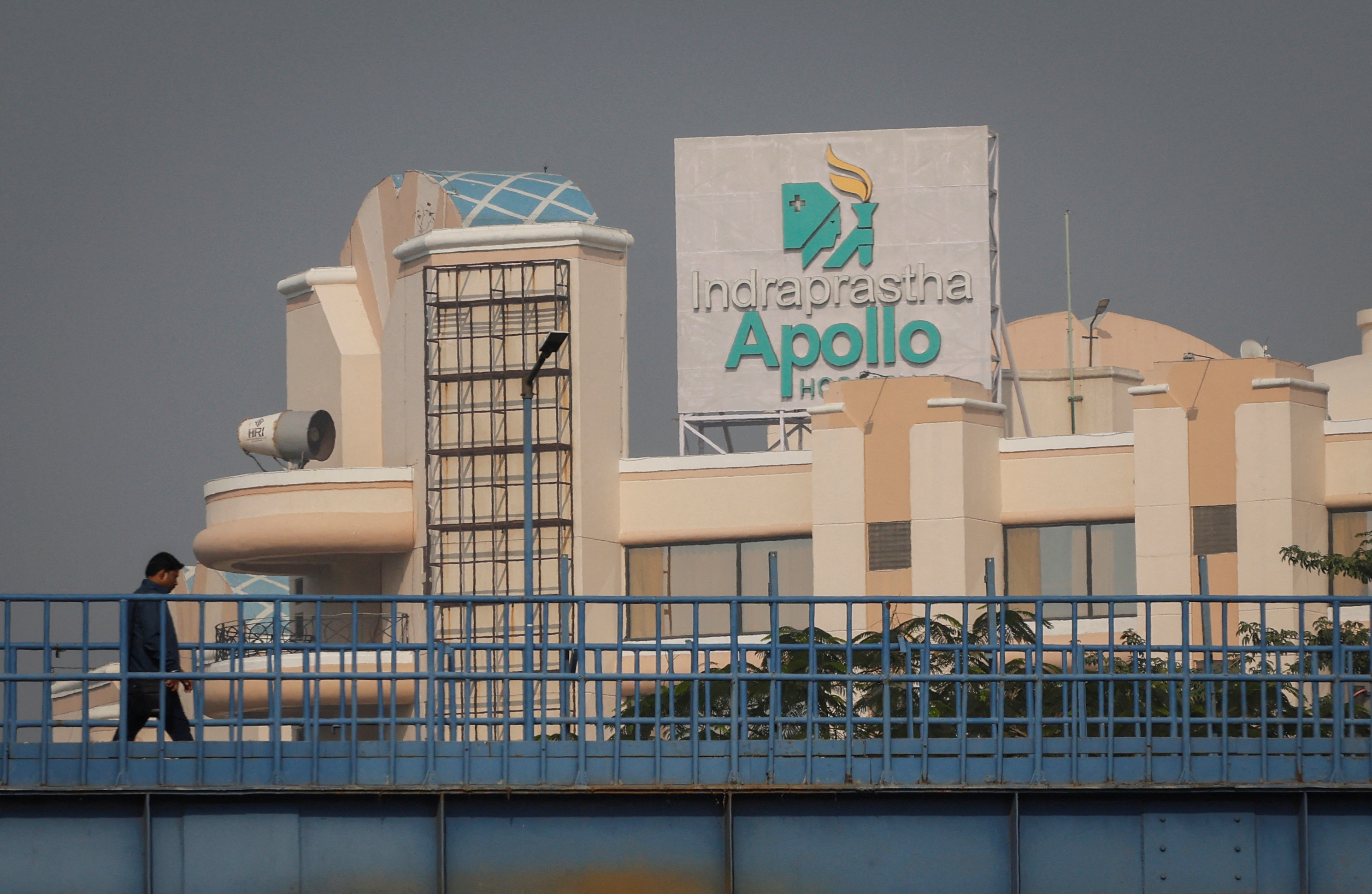 A man walks on a pedestrian bridge in front of an Apollo hospital building in New Delhi