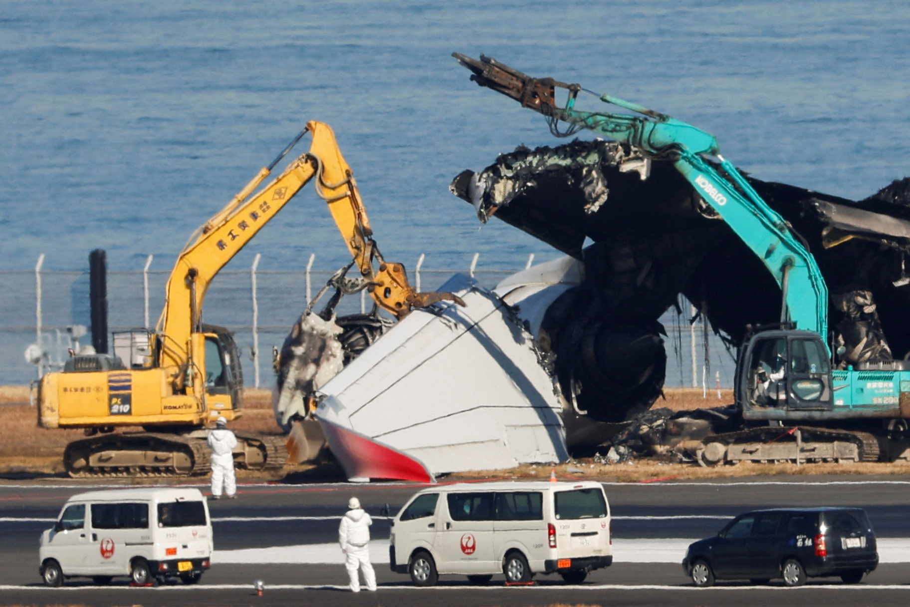 Officials try to remove the wreckage of a burnt JAL Airbus A350 plane after a collision with a Japan Coast Guard aircraft, in Tokyo