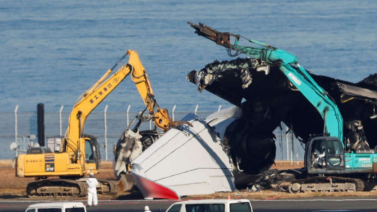 Officials try to remove the wreckage of a burnt JAL Airbus A350 plane after a collision with a Japan Coast Guard aircraft, in Tokyo