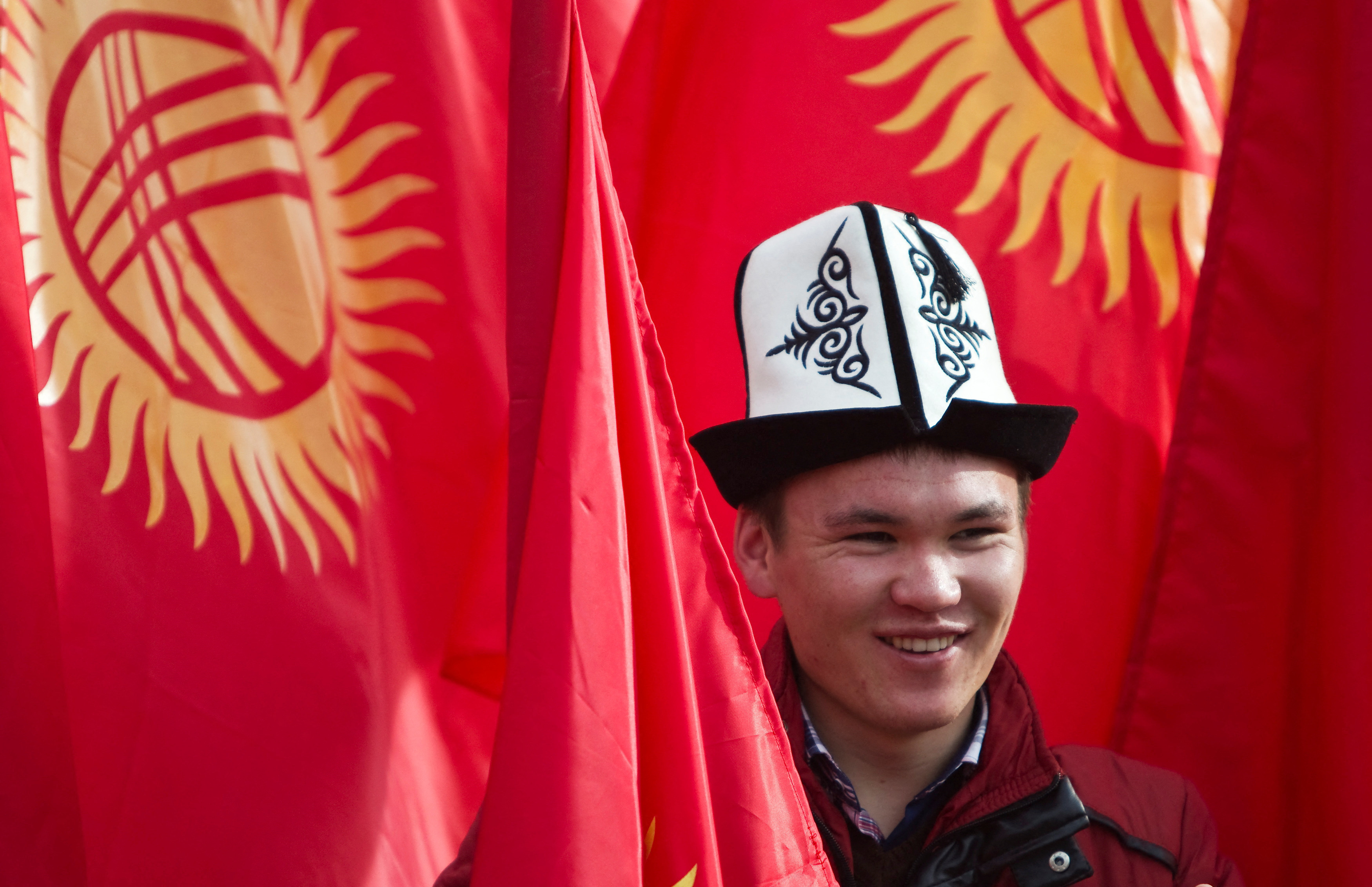 Man wearing a Kyrgyz national hat poses with national flags in Bishkek