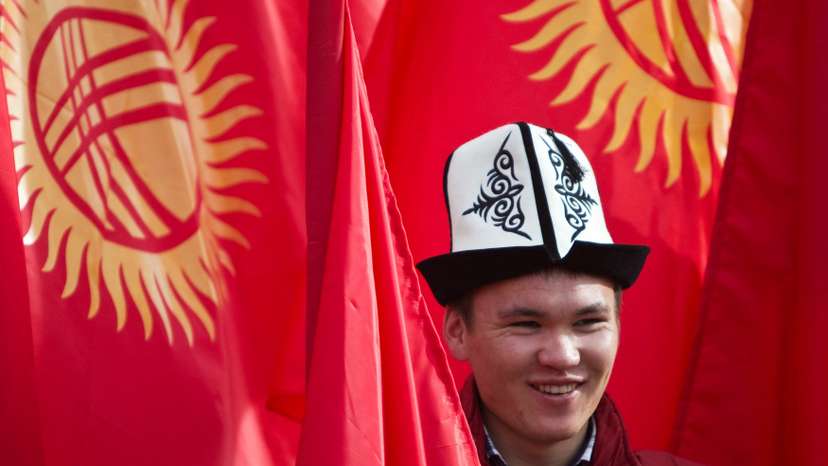 Man wearing a Kyrgyz national hat poses with national flags in Bishkek