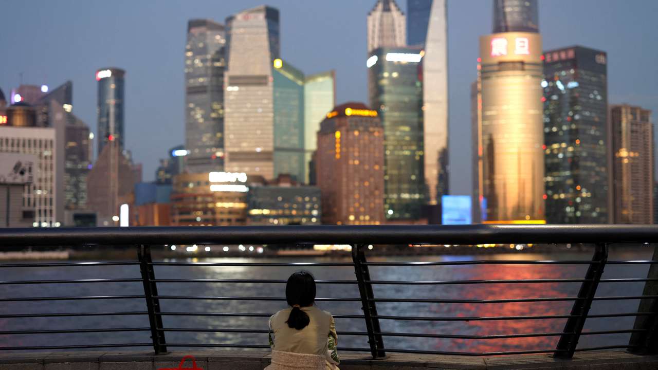 Woman sits one the Bund near Huangpu river as she looks on the financial district of Pudong in Shanghai