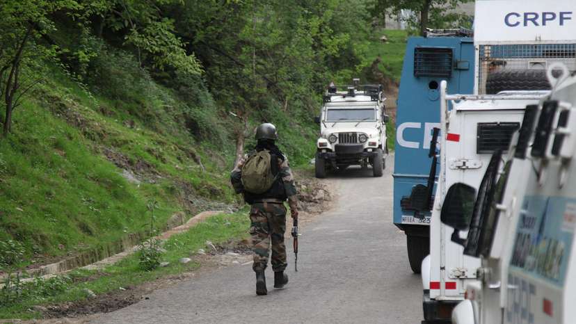 An Indian security force trooper moves past parked vehicles during a cordon and search operation, in Gudder village
